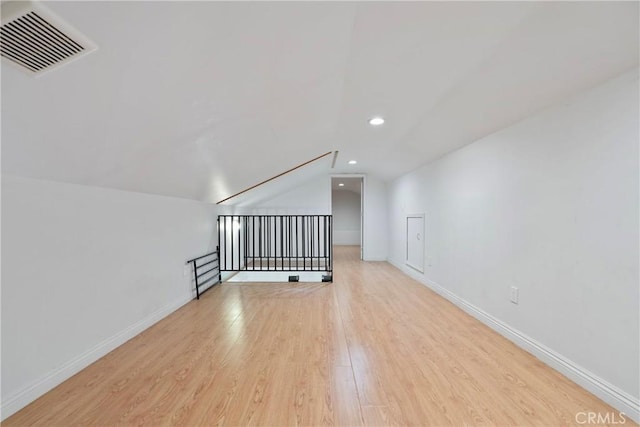 additional living space featuring visible vents, baseboards, light wood-style flooring, vaulted ceiling, and recessed lighting