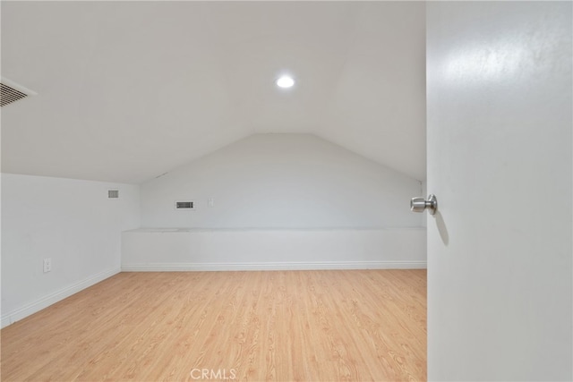 additional living space featuring light wood-style flooring, visible vents, vaulted ceiling, and baseboards