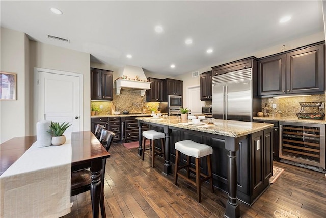 kitchen with beverage cooler, visible vents, an island with sink, dark wood-style flooring, and built in appliances