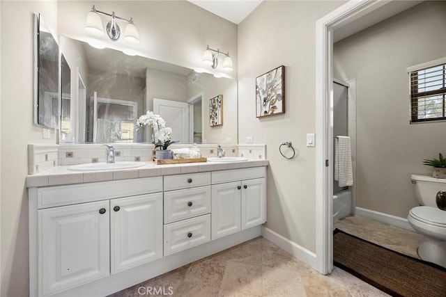 bathroom with double vanity, toilet, baseboards, and a sink