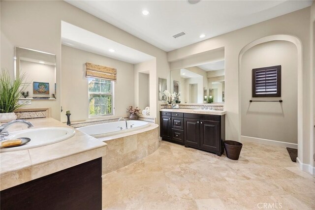 full bath featuring two vanities, a bath, visible vents, and a sink