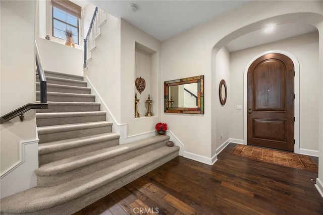 entrance foyer featuring baseboards, arched walkways, dark wood-style flooring, and stairway