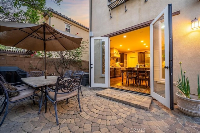 patio terrace at dusk featuring a grill, outdoor dining space, and fence