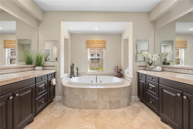 bathroom featuring a bath, a sink, a wealth of natural light, and two vanities