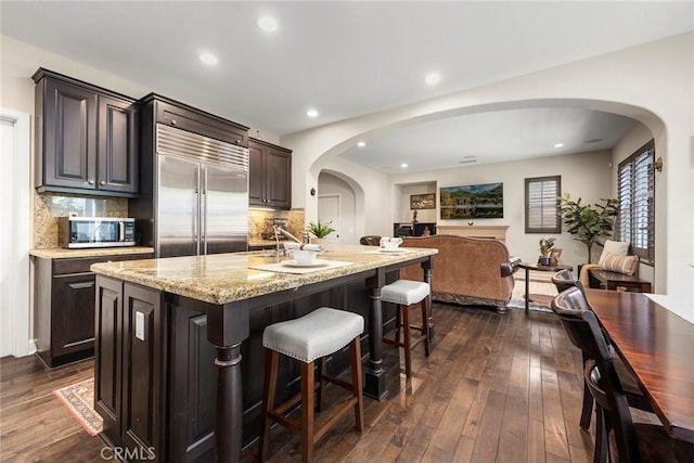 kitchen featuring a kitchen bar, light stone counters, dark wood-style floors, and stainless steel appliances