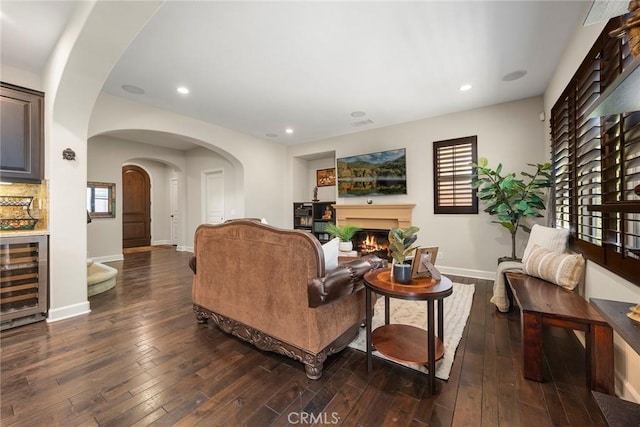 living room with hardwood / wood-style floors, beverage cooler, baseboards, and a lit fireplace