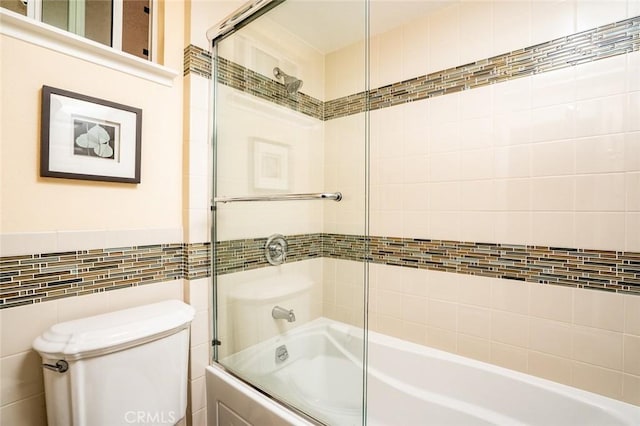 full bath with tile walls, toilet, and bath / shower combo with glass door