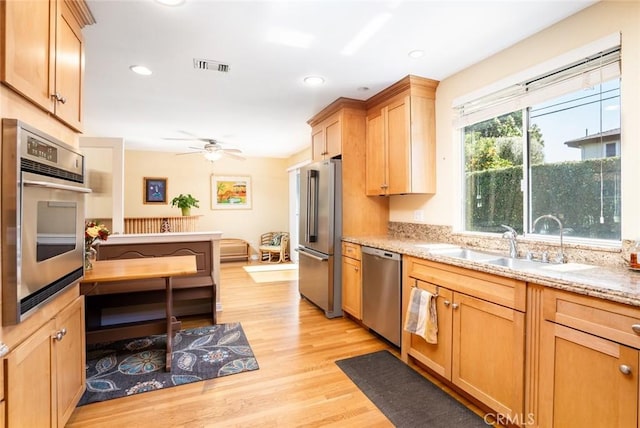 kitchen with light wood finished floors, visible vents, appliances with stainless steel finishes, light stone counters, and a sink