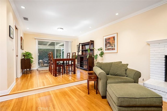 living room featuring ornamental molding, light wood finished floors, a fireplace, and visible vents