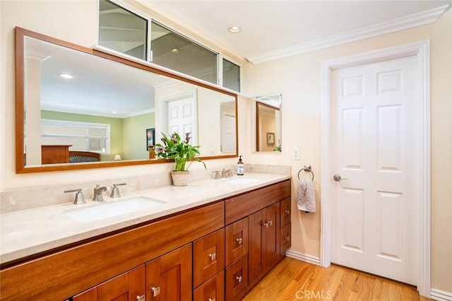 bathroom with double vanity, crown molding, a sink, and wood finished floors