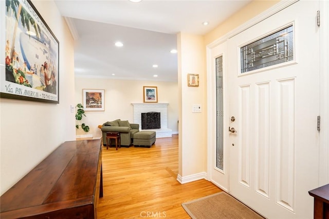 entrance foyer featuring a fireplace, recessed lighting, light wood-style flooring, ornamental molding, and baseboards