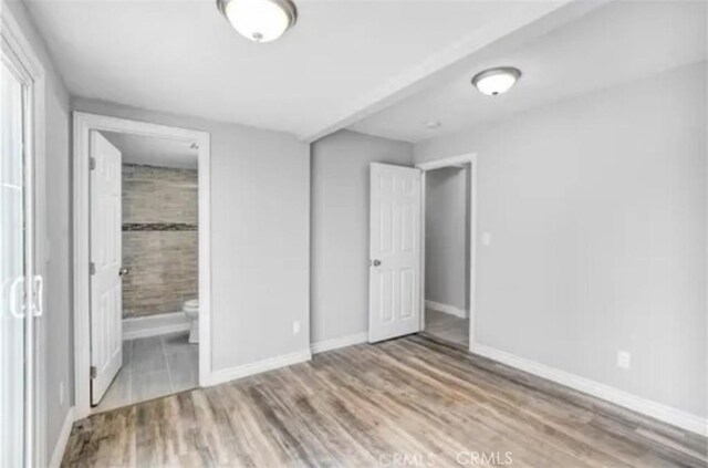 unfurnished bedroom featuring ensuite bath, baseboards, and wood finished floors