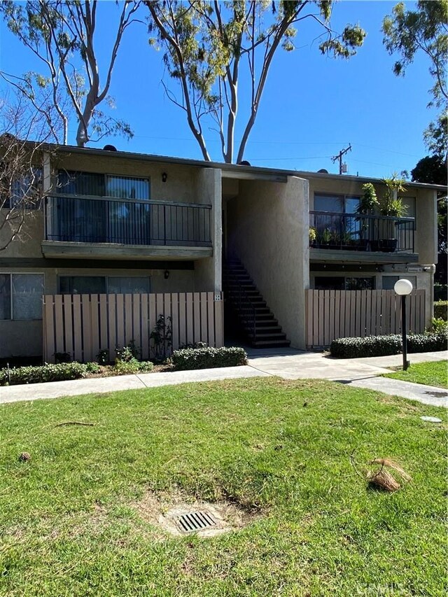 view of front of property featuring stairway, a front yard, a balcony, and stucco siding