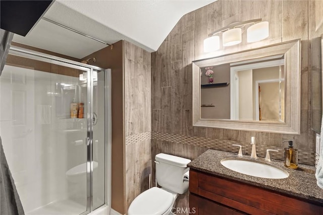 bathroom featuring a stall shower, toilet, vaulted ceiling, vanity, and tile walls