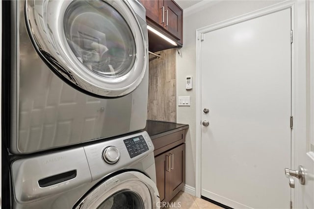 clothes washing area featuring cabinet space, stacked washer / drying machine, and light tile patterned flooring