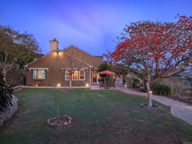 rear view of house with a chimney, a lawn, and a patio