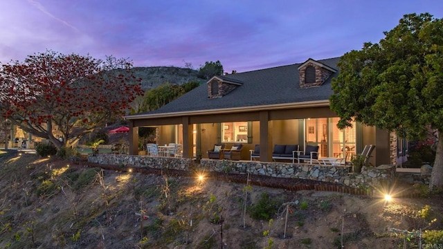 back of house at dusk with an outdoor hangout area and a patio