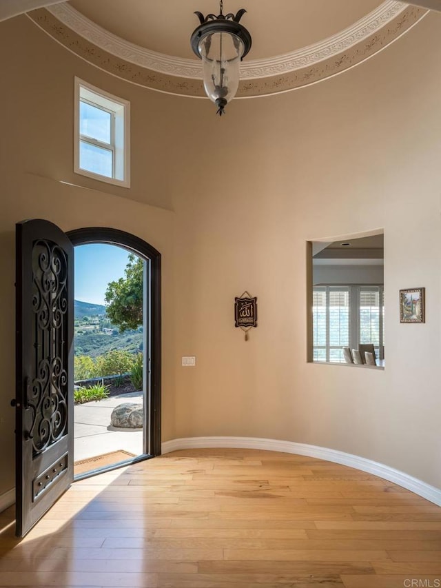 foyer with crown molding, a towering ceiling, baseboards, and wood finished floors