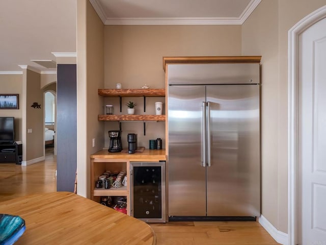 kitchen with arched walkways, wine cooler, ornamental molding, stainless steel built in refrigerator, and light wood-type flooring