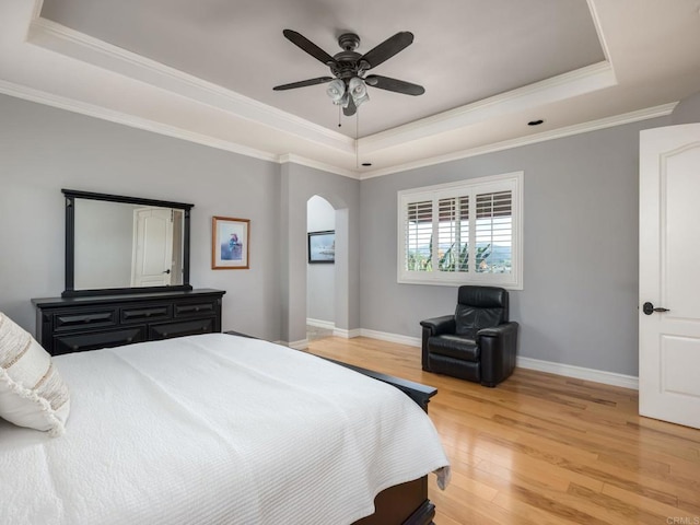 bedroom with light wood-style flooring, arched walkways, a raised ceiling, and baseboards