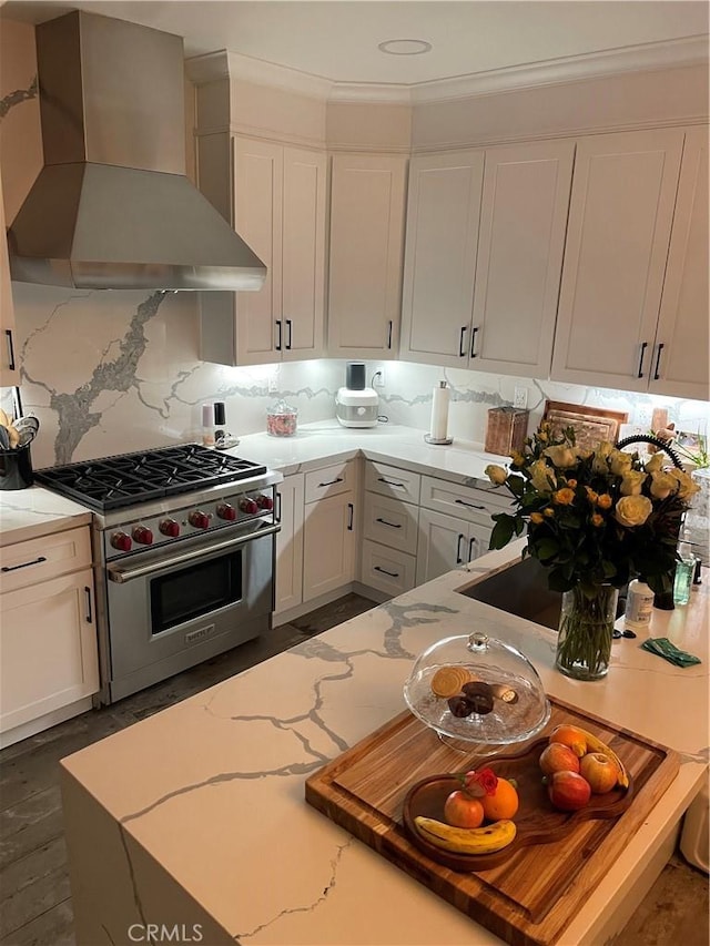 kitchen featuring tasteful backsplash, white cabinetry, premium range, wall chimney range hood, and light stone countertops