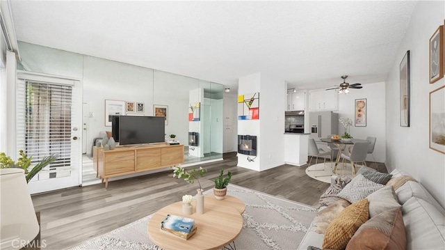 living room featuring ceiling fan, wood finished floors, and a glass covered fireplace