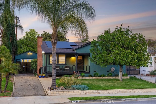 view of front of home with a porch, solar panels, fence, stucco siding, and a front yard