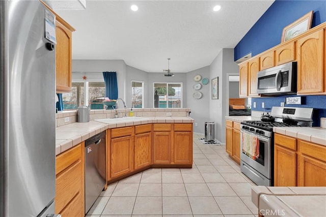 kitchen with appliances with stainless steel finishes, a sink, tile countertops, and a peninsula