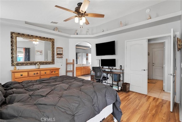 bedroom featuring arched walkways, visible vents, a tray ceiling, light wood finished floors, and ensuite bath