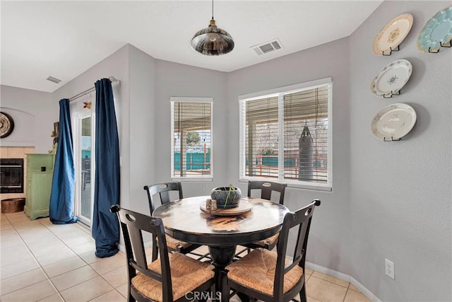 dining area featuring baseboards, visible vents, a tiled fireplace, and light tile patterned flooring