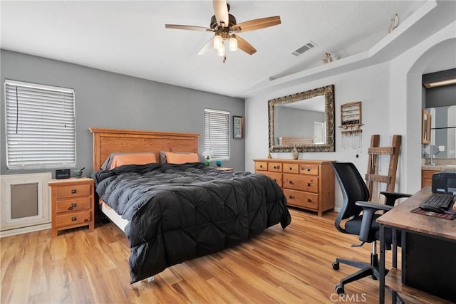 bedroom with arched walkways, visible vents, light wood-style flooring, vaulted ceiling, and ceiling fan