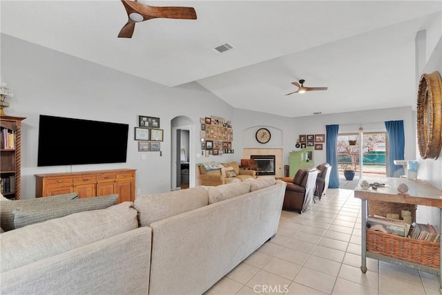 living area with light tile patterned floors, lofted ceiling, a fireplace, visible vents, and a ceiling fan