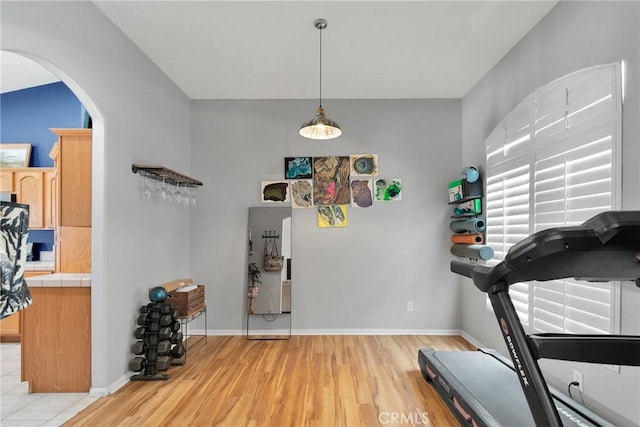 workout room with arched walkways, light wood-type flooring, and baseboards