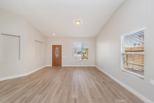 unfurnished room with lofted ceiling, light wood-type flooring, and baseboards