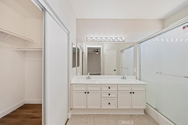 bathroom featuring a walk in closet, a shower with shower door, a sink, and double vanity