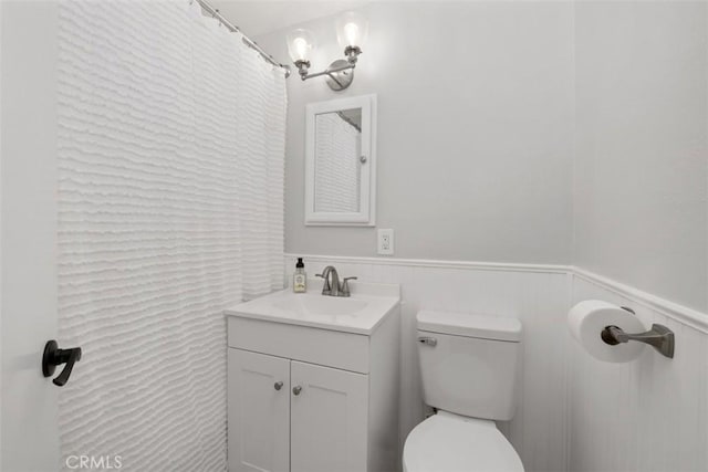 bathroom with a wainscoted wall, toilet, and vanity