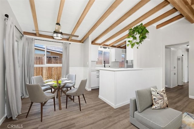 dining area with a wainscoted wall, vaulted ceiling with beams, and light wood finished floors