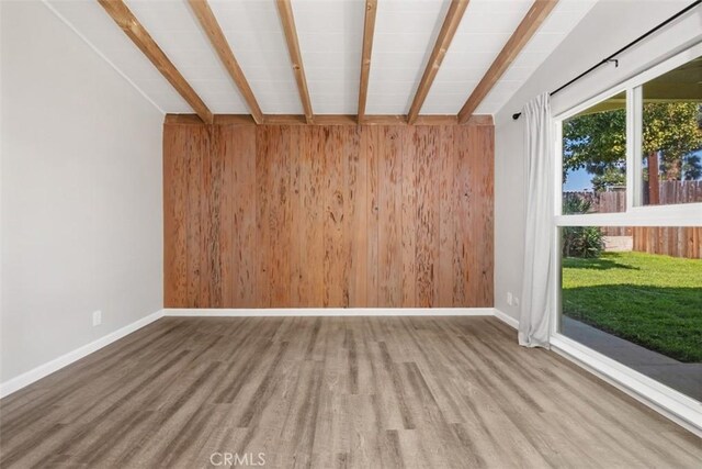 empty room with wood walls, wood finished floors, and baseboards