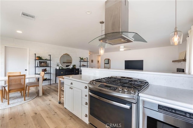 kitchen with island exhaust hood, light countertops, visible vents, gas stove, and white cabinets