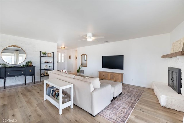 living room featuring a fireplace with raised hearth, light wood-type flooring, and a ceiling fan