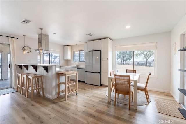 kitchen with stainless steel appliances, a sink, visible vents, light wood-style floors, and island exhaust hood