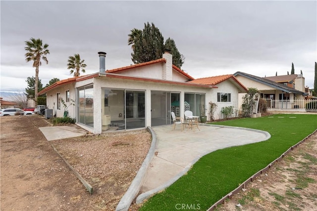 back of property featuring a lawn, a sunroom, a chimney, a patio area, and stucco siding