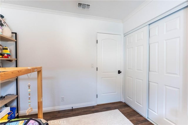 bedroom with baseboards, visible vents, dark wood-type flooring, crown molding, and a closet