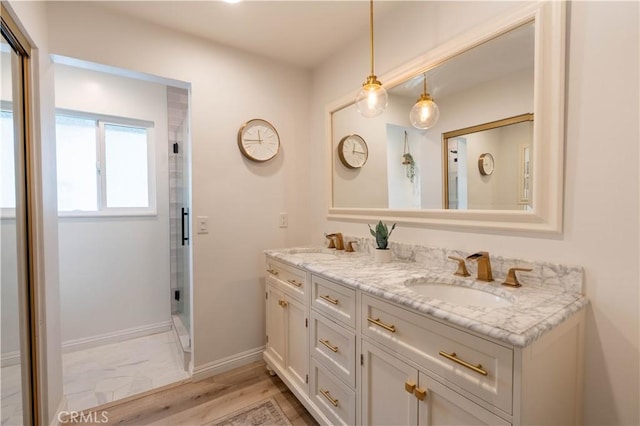 full bathroom with double vanity, a shower stall, baseboards, and a sink