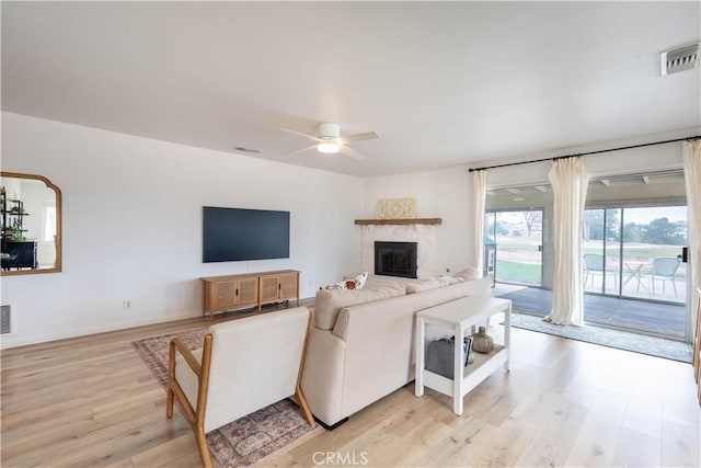 living area with a fireplace, a ceiling fan, baseboards, visible vents, and light wood-style floors