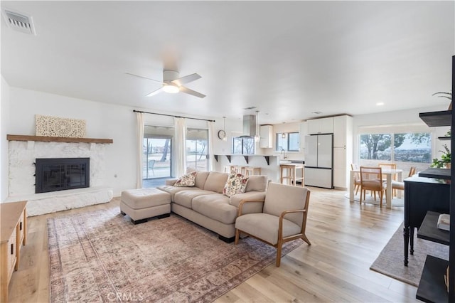 living room featuring light wood finished floors, plenty of natural light, a glass covered fireplace, and visible vents