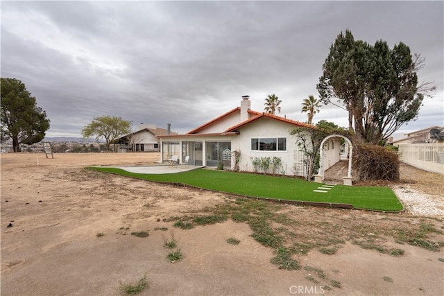 rear view of house with a patio, a chimney, stucco siding, a lawn, and fence