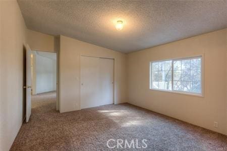 unfurnished bedroom with a textured ceiling, carpet floors, and vaulted ceiling