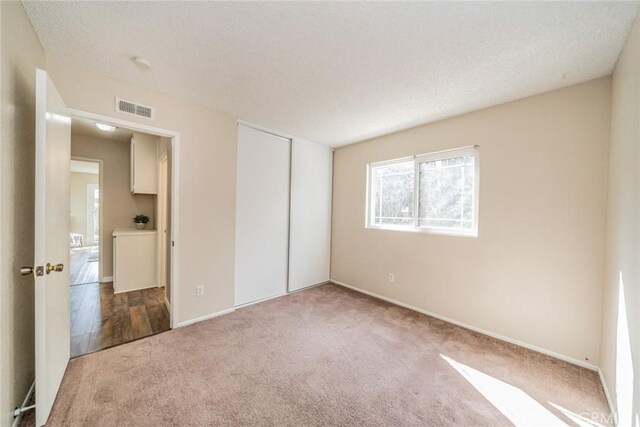 unfurnished bedroom with a closet, visible vents, a textured ceiling, and carpet