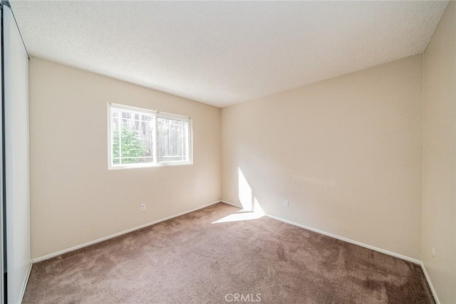 carpeted empty room featuring a textured ceiling and baseboards